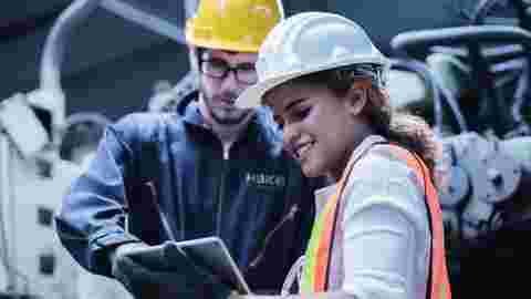 Engineers from HBK, with helmets, in a factory looking for a laptop regarding their Services.