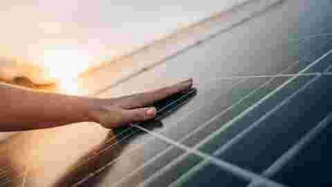 Close-up of human hand touching solar panel during Sunset