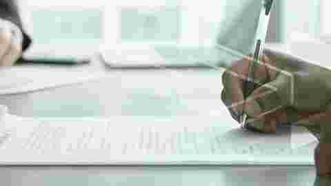 two men seated at a meeting desk signing papers about the Terms and Conditions